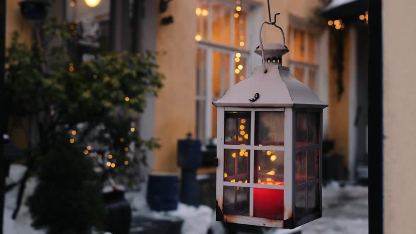 A soft glow from a lantern illuminates a winter evening, surrounded by twinkling lights and snow.