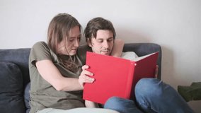 Smiling loving couple sitting together on sofa at home, reading red book, sharing cozy moments - Powered by Shutterstock - Get 15% off with code: PIKWIZARD15