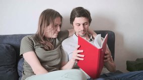 Smiling loving couple sitting together on sofa at home, reading red book, sharing cozy moments - Powered by Shutterstock - Get 15% off with code: PIKWIZARD15