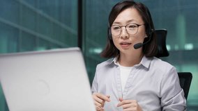 Confident asian businesswoman in wireless headset talking on video call conference using a laptop sitting in office. Female coach speaks remotely, communicates at online meeting or training. Close up - Powered by Shutterstock - Get 15% off with code: PIKWIZARD15