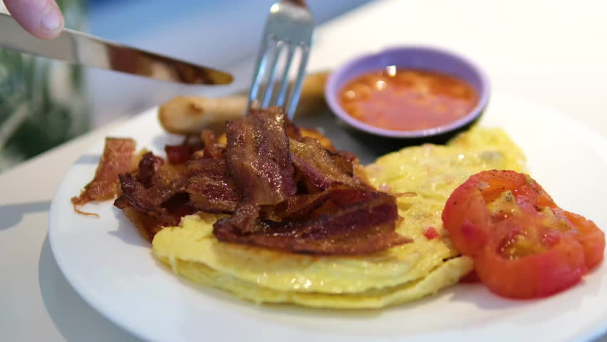 Bacon omelette tomato Cutting into a fluffy omelette on a plate