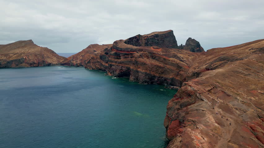 Drone spectacular ocean rocks washed by blue ocean. Tranquil sea cliffs contrasting with vast sea. Rippling water washing rough volcanic formation at cloudy sky. Serene picturesque seascape outdoors