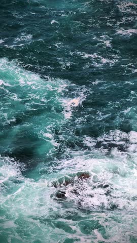 Macro-like close-up of Atlantic Ocean water at the base of Kerry Cliffs, Ireland, on a windy sunny day with moving clouds and spray from rugged coastline.