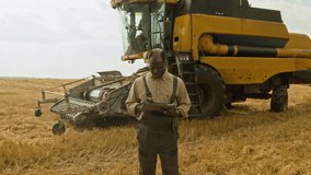 Two farmers working in wheat field African American man using digital tablet while combine operator climbing into cabin in background, copy space - Powered by Shutterstock - Get 15% off with code: PIKWIZARD15