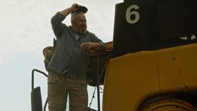 Medium shot of African American man as smiling farmer looking at camera and using digital tablet while standing in wheat field with combine harvester in background, copy space - Powered by Shutterstock - Get 15% off with code: PIKWIZARD15