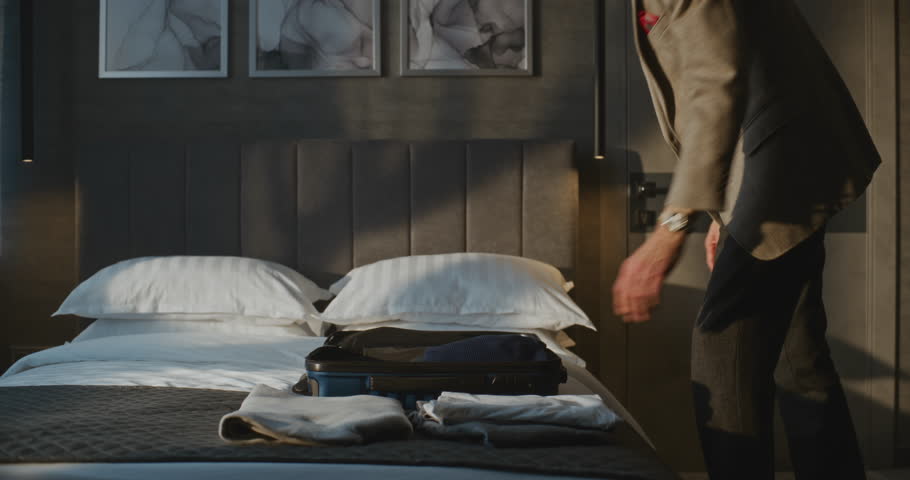 Elegant Gray Haired Man Meticulously Packs Clothes Into Small Blue Suitcase. Man Checking Out of Hotel in Hurry to Catch Flight. Concept of Travel, Routine of Traveler, Business Trip. Static Shot.