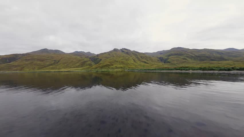 Dynamic flight over the sea with opening views of mounyains and green coastline of Alaska. Unalaska island, aerial view of quiet bay and natural beauty. Dutch Harbor, Aleutians Islands, Alaska.