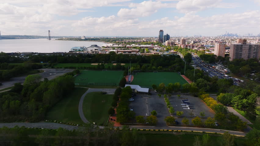 Aerial view of John Paul Jones Park and athletic fields near Shore Parkway with Verrazzano-Narrows Bridge and Manhattan skyline in distance, Brooklyn, New York. ProRes HQ422.