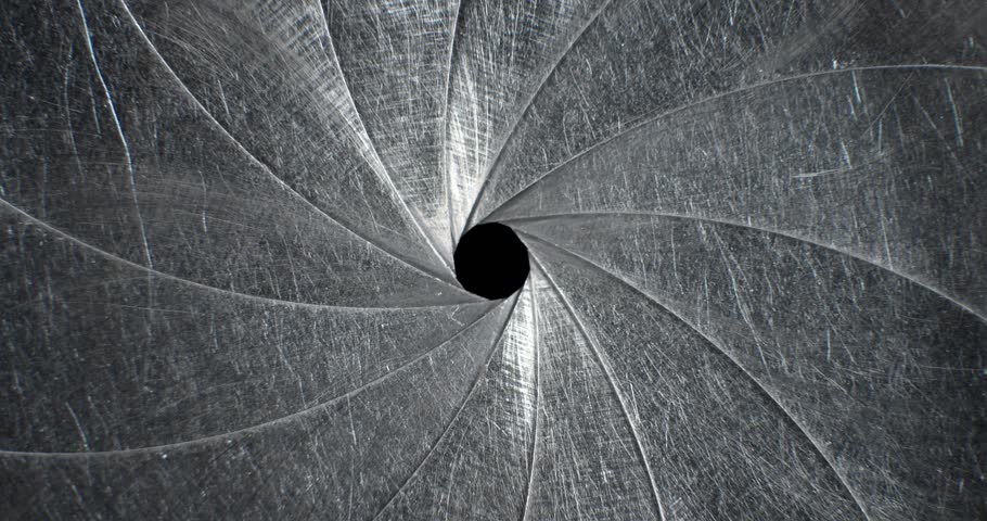 Circular blades of a mechanical iris create a precision opening controlling amount of light entering a camera lens with the opening mechanism controlling the aperture and the depth of field in focus.