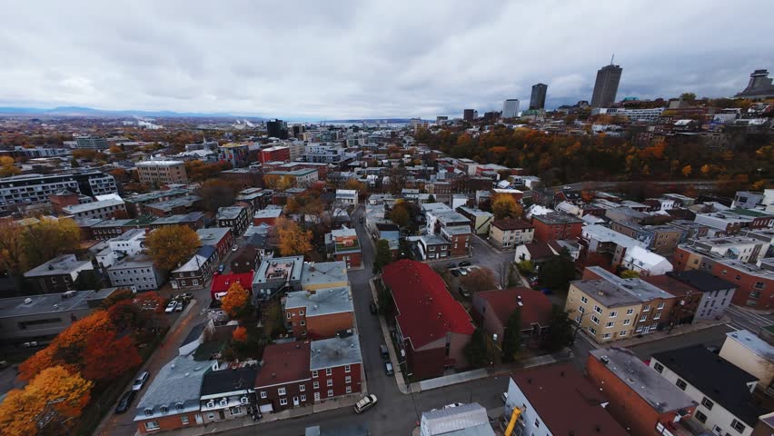 Aerial 4K drone view of Quebec City skyline after rain—moody clouds, autumn trees and dense urban blocks along the St. Lawrence horizon.