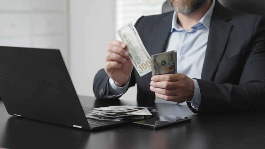 Businessman counting money at desk. Financial success and profit concept. Cash and online banking background. Man managing income and savings. Wealth and investment management scene.