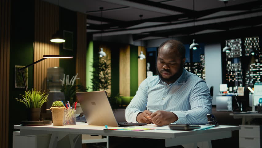 Black office employee ripping a piece of paper after making a mistake, restarting his task in anger and tearing up the page sheet. Discontent guy writes a typo while transcribing. Camera A.