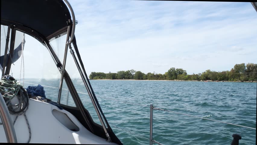 Panning across the horizon standing at the helm of a sailboat looking through the dodger at the sails.
