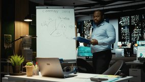 Black businessman scribbling monthly insights and reports on a white board, making projections with candlestick charts using data analysis. Forecasting data to achieve revenue targets. Camera A. - Powered by Shutterstock - Get 15% off with code: PIKWIZARD15