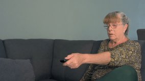 Elderly woman smiling watching TV eating popcorns sitting on the couch at home - Powered by Shutterstock - Get 15% off with code: PIKWIZARD15