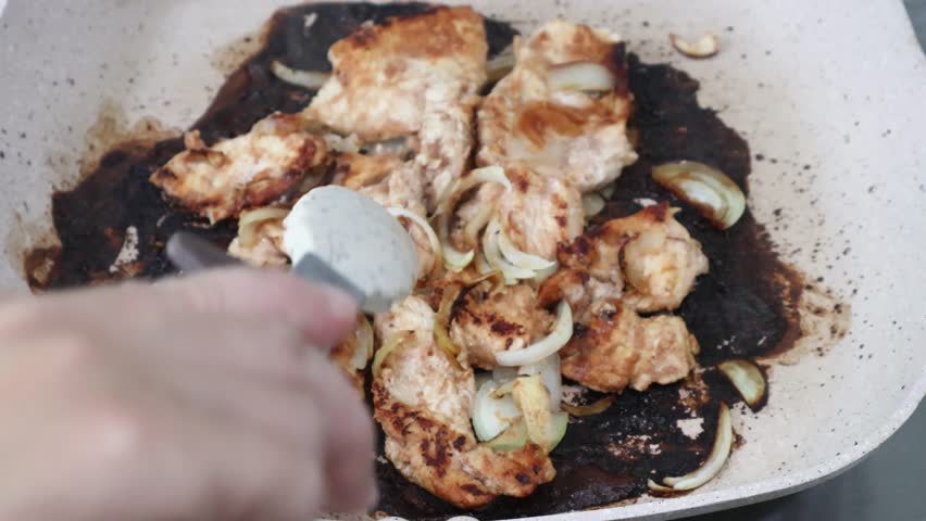 Cooked chicken breast fillets and caramelized onion slices flipped in a hot pan with tongs. Close up of the final stage of grilling, showing the ready-to-eat meal.