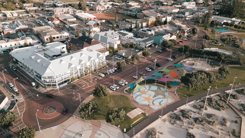 Aerial footage at sunset in Geraldton, Perth, Western Australia. The footage first shows some business and residential buildings, and then slowly pans over to the sandy beaches and ocean waves.