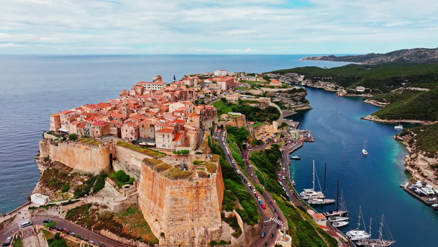 Aerial drone shot over the historic coastal town of Bonifacio in Corsica, France. High view of the rocky steep cliff and the turquoise sea. Ancient Citadel overlooking the rugged coastline.