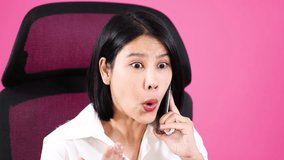 Shocked, frustrated woman in white shirt on phone, seated against a pink office background. - Powered by Shutterstock - Get 15% off with code: PIKWIZARD15
