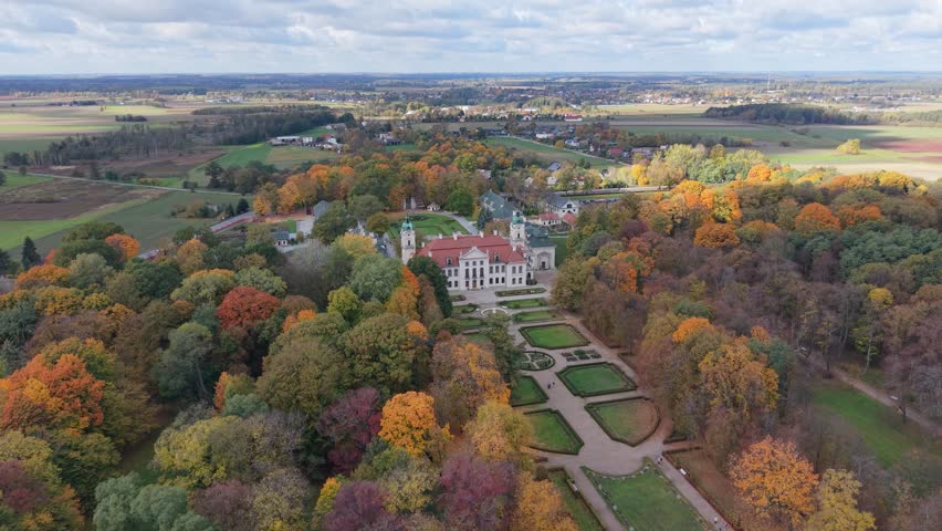 Aerial drone orbit showing the backside view of the historic Zamoyski Palace surrounded by trees in Kozlowka, Poland.
