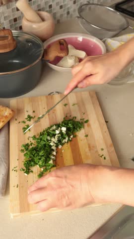Anonymous person chops parsley and garlic on kitchen table at home. Healthy eating and traditional cuisine. Seasonal farm products.
