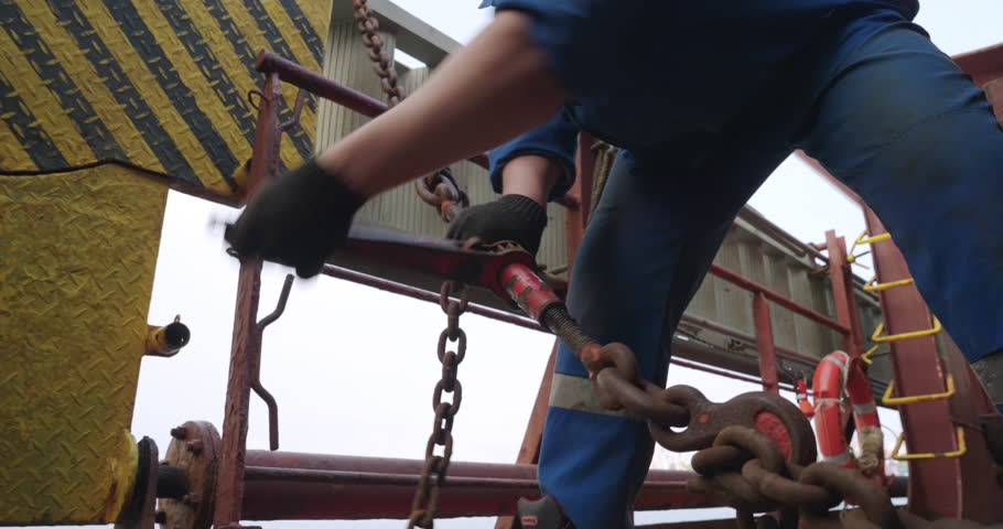 Worker handles heavy chains aboard ship and metal links clanging softly on dock. Metallic shining chains swing slowly in coordinated rhythm