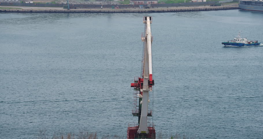 Motion of ship mirrors stillness of mechanical giant. Steel geometry reflecting on tranquil water. Harbor rests under soft evening light