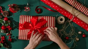 Top view of female hands holding a beautifully wrapped Christmas gift in kraft paper with a shiny red satin bow. Festive decorations surround the gift, creating a warm and joyful holiday atmosphere. - Powered by Shutterstock - Get 15% off with code: PIKWIZARD15