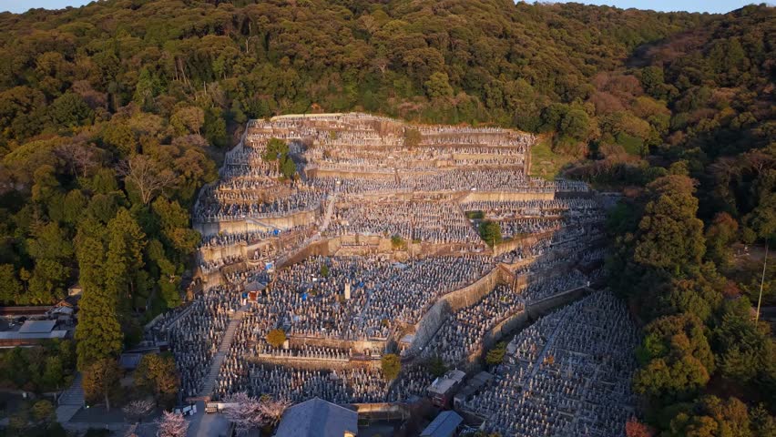 Aerial drone view of the Higashi Otani Cemetery in Kyoto, Japan, in daylight. Expansive traditional graveyard surrounded by trees and temples, showcasing Japanese heritage.