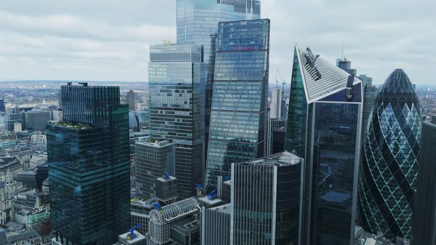 Aerial view of towering skyscrapers pierce the overcast sky, their glass facades reflecting the urban landscape, London, United Kingdom.
