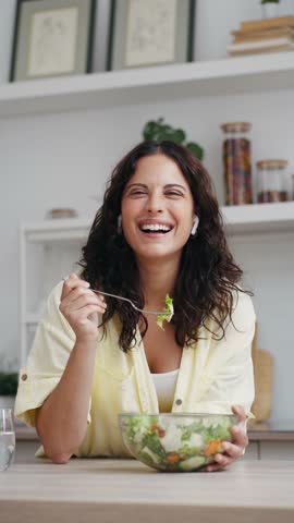 Video of beautiful woman eating healthy salad while looking at camera in the kitchen at home