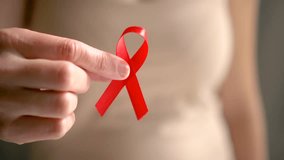 Close up of woman hand holding red ribbon. Symbol of AIDS and HIV awareness, health prevention, and global support. December month of compassion and protection for infected people. - Powered by Shutterstock - Get 15% off with code: PIKWIZARD15