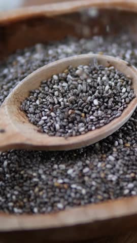Close up shot of nutritious chia seeds falling slowly into a rustic wooden spoon placed in a bowl, highlighting the concept of superfoods and healthy eating for a balanced diet