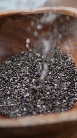 Nutritious black and white chia seeds slowly falling into a rustic wooden bowl, showcasing a superfood ingredient popular in healthy eating, vegan diets, and for its antioxidant benefits