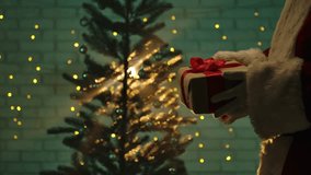A festive scene featuring a Santa Claus figure holding a wrapped Christmas gift with a red ribbon in front of a beautifully lit Christmas tree. - Powered by Shutterstock - Get 15% off with code: PIKWIZARD15