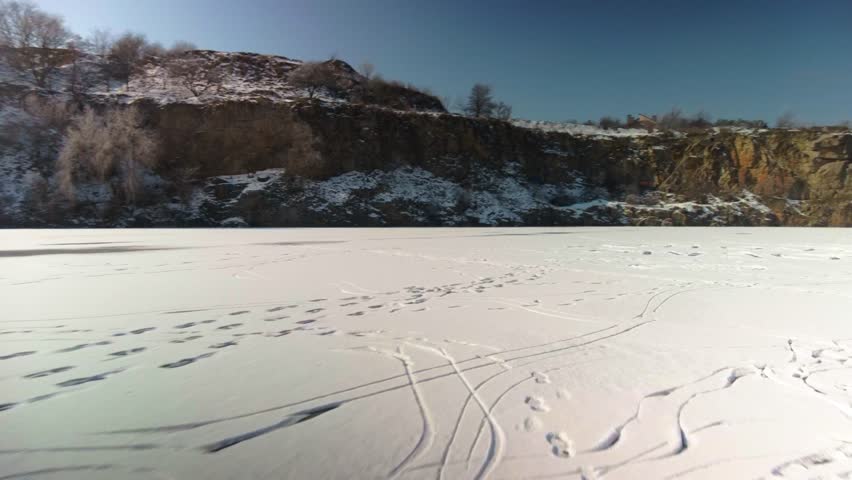 Traces of figure skates sliding on ice surface at nature. POV gliding on ice, scenic snowy landscape and rocky hills, active winter recreation