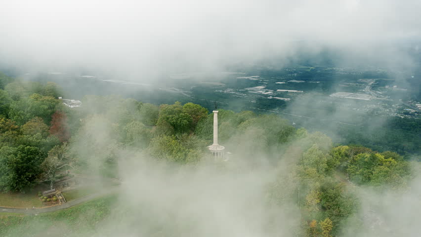 The Point Park statue emerges through thick mountain fog in a wide drone shot revealing the sweeping valley below.