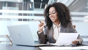 Happy african american businesswoman satisfied with financial results sitting in office. Smiling female financier looks at documents and computer, rejoices at positive indicators, celebrates success - Powered by Shutterstock - Get 15% off with code: PIKWIZARD15