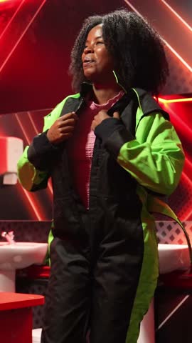 Happy african american woman laughing and excitedly getting dressed in a black and neon green racing suit, preparing for a go kart race