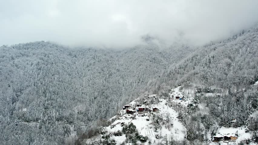 A drone view capturing the charm of winter in Turkey — a snowy mountain village with wooden houses surrounded by white forests and peaceful natural beauty.