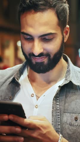 A man smiles as he uses a dark-themed smartphone app at night in the city, absorbed in the digital experience.