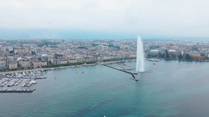 Aerial view of the Jet d'Eau de Genève, a tall water fountain in the middle of the lake, surrounded by a city skyline and boats, Geneva, Switzerland.