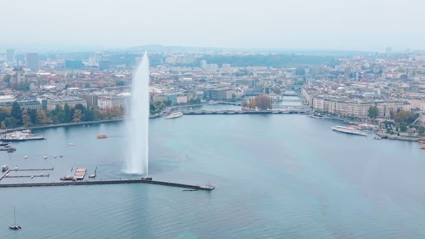 Aerial view of the Jet d'Eau de Genève shooting a powerful stream of water, contrasting with the muted tones of the cityscape, Geneva, Switzerland.