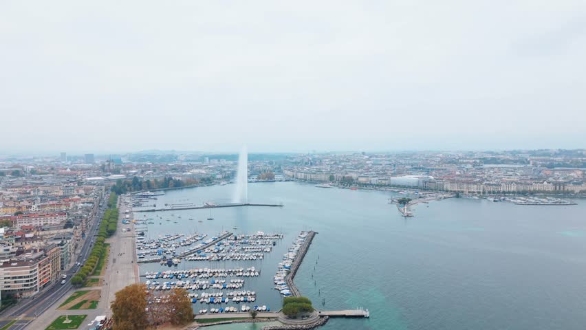 Aerial view of the iconic Jet d'Eau fountain shooting high into the sky near the marina filled with boats, along Quai Gustave-Ador, Geneva, Switzerland.