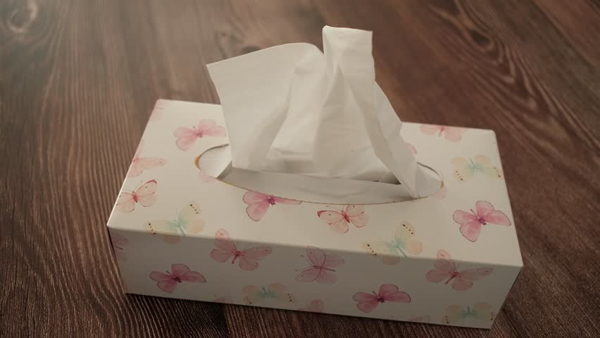 A box of tissues with butterflies on it sits on a wooden floor. The box is open and the tissues are white