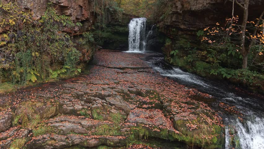 Peaceful woodland scene with a waterfall and vibrant autumn foliage in Wales
