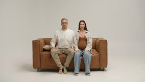 A serious-looking man and woman on a brown sofa in a minimalist white room. They look at the camera, then at each other, creating a tense, cinematic moment. - Powered by Shutterstock - Get 15% off with code: PIKWIZARD15