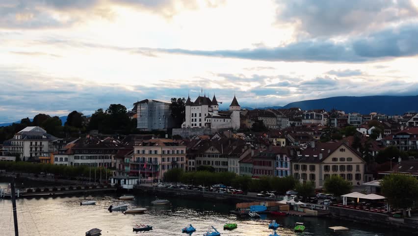 Aerial view of Nyon Castle, its imposing medieval architecture contrasting with the charming townscape below, under a cloudy sky, Nyon, Vaud, Switzerland.
