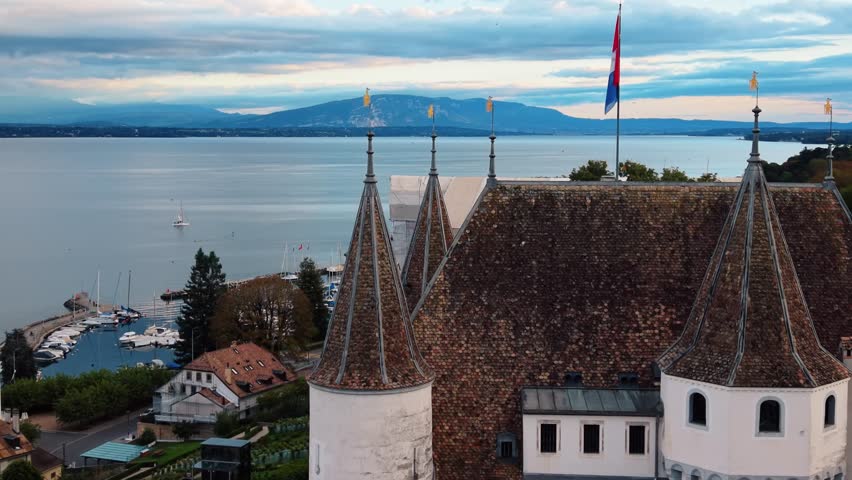 Aerial view of the magnificent Nyon Castle, its flag fluttering proudly amidst the backdrop of the serene lake, Nyon, Vaud, Switzerland.