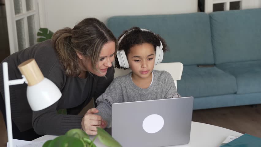 Caucasian mother and African American daughter studying at home, mom teaching math doing homework in cosy white room. Parent teach, child school girl learn mathematics, write exercise read book